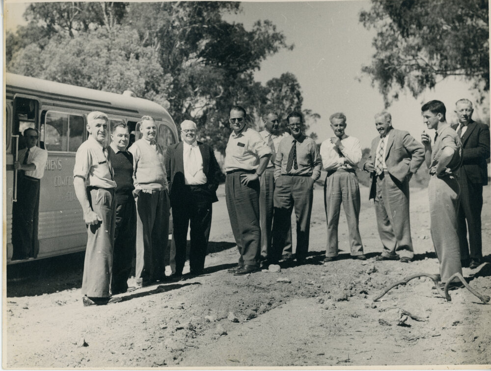 Group of men looking at dirt road with bus in background 