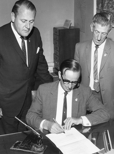 Shire President P.G. Hosking signing the petition to have Frankston declared a city. Accompanied by George Pentland (Shire Secretary) and Cr Eric Bell, the second signatory to the petition.